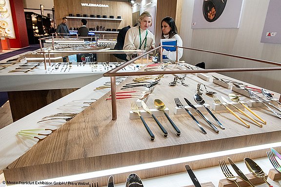 Besteck-Ausstellung auf der Messe Frankfurt, mit verschiedenen Messern, Gabeln und Löffeln, die auf einem stilvollen Holztisch präsentiert werden.